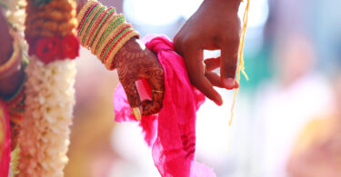 Mãos unidas por um pano rosa em um casamento hindu.