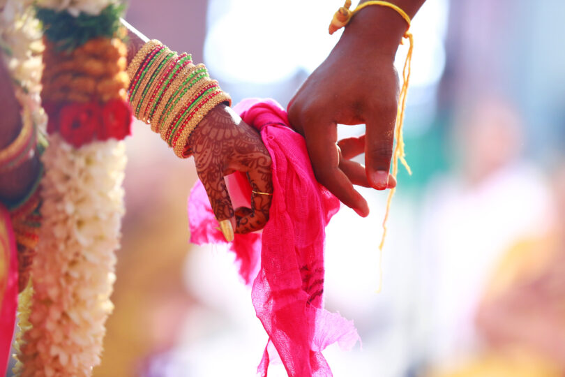 Mãos unidas por um pano rosa em um casamento hindu.