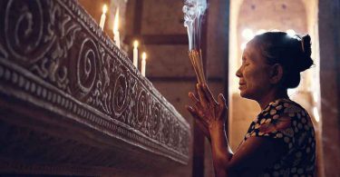Mulher segurando incensos em sinal de oração dentro de um templo.
