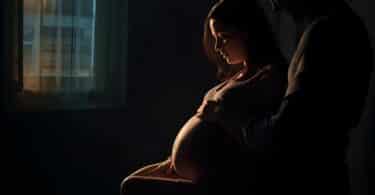 Imagem de uma mulher grávida sentada em uma cadeira e ao lado o seu esposo. Ela está quase entranda em trabalho de parto.