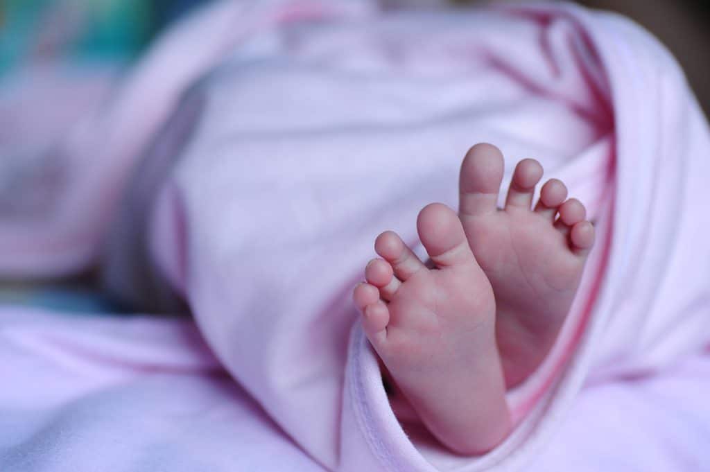 Pezinhos de um bebê que está enrolado em uma manta rosa.