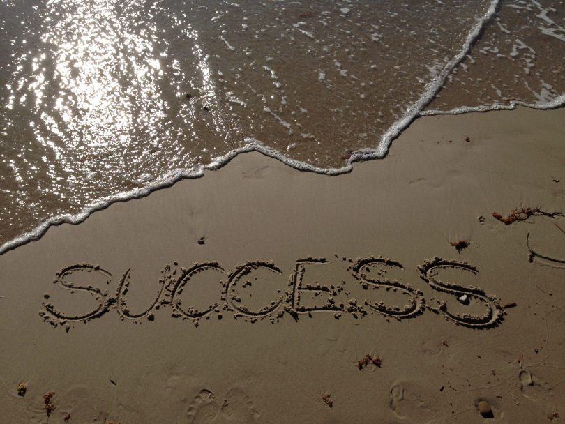 "Success" escrito na areia com água do do mar ao lado