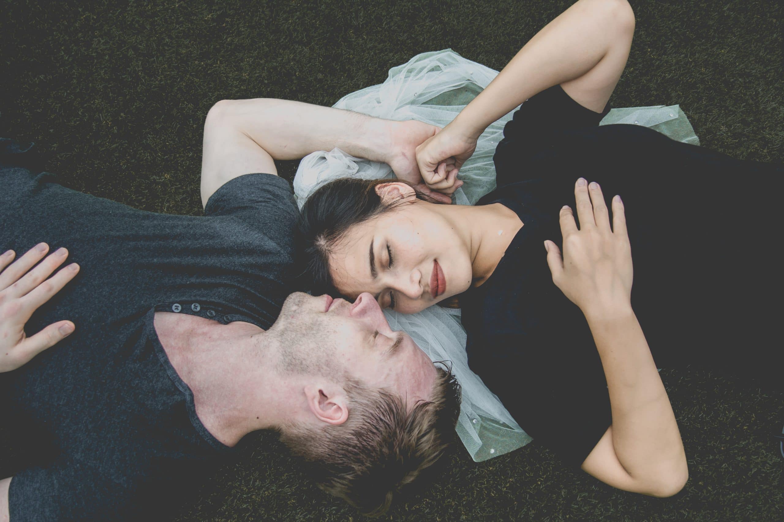 Casal deitado na grama visto de cima com as mãos datas e olhos fechados