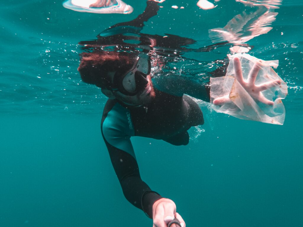 Homem mergulhando e pegando um pedaço de sacola de plástico que está no oceano.