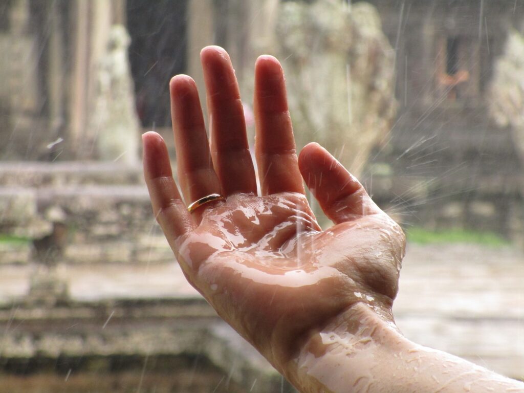 Uma mão estendida onde nela caem gotas de chuva.