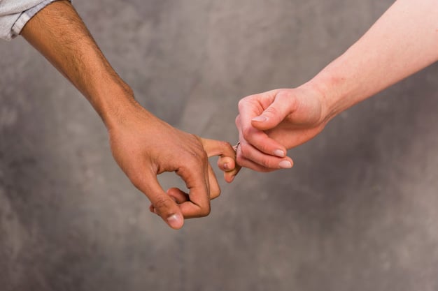 Mão de um homem com o dedo mindinho entrelaçado com o de uma mulher.