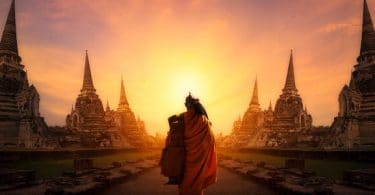 Monge caminhando entre templos em direção ao pôr-do-sol.