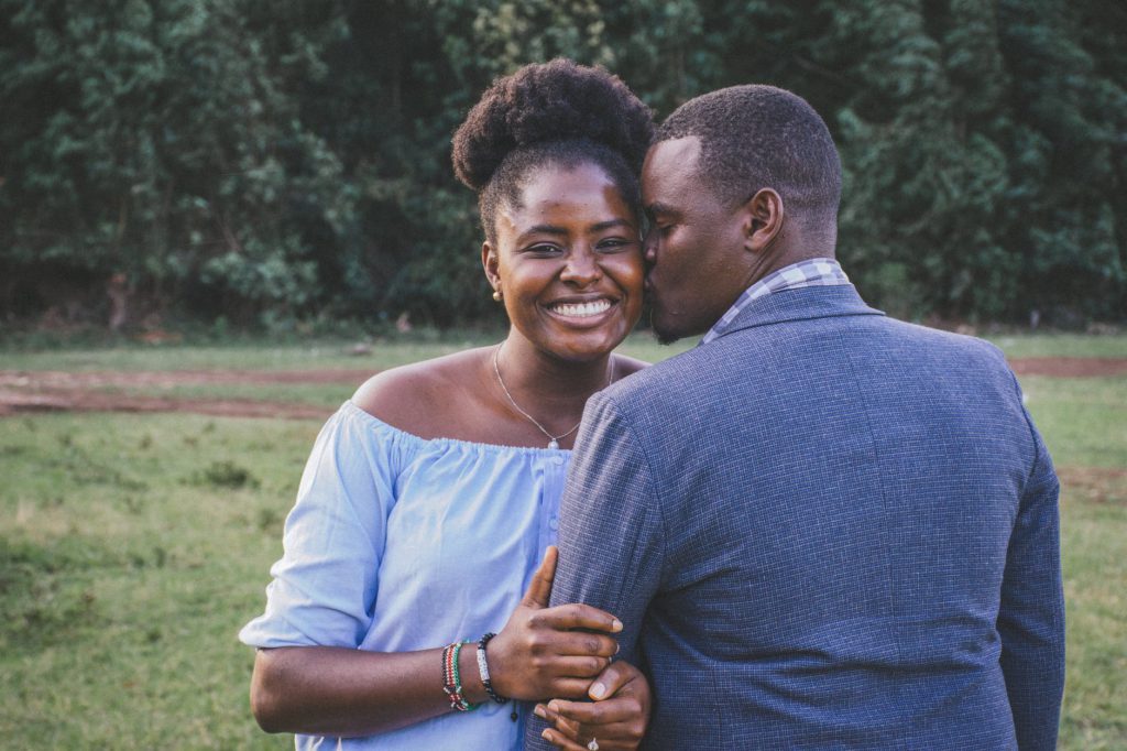 Casal de homem e mulher, ambos negros, sorridentes e se abraçando. 