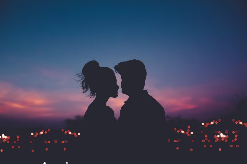 Silhueta de casal de homem e mulher, se encarando frente a frente, posando em uma paisagem urbana, no anoitecer