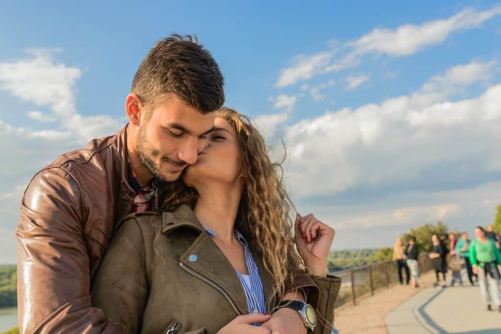 Casal se abraçando enquanto a mulher dá um beijo na bochecha do companheiro. 