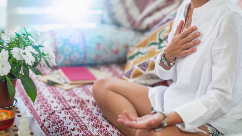 Mulher sentada com a mão no peito, representando meditação e cura