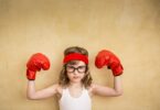 Menina com luvas de boxe e as mãos levantadas em sinal de força.