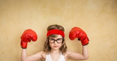 Menina com luvas de boxe e as mãos levantadas em sinal de força.