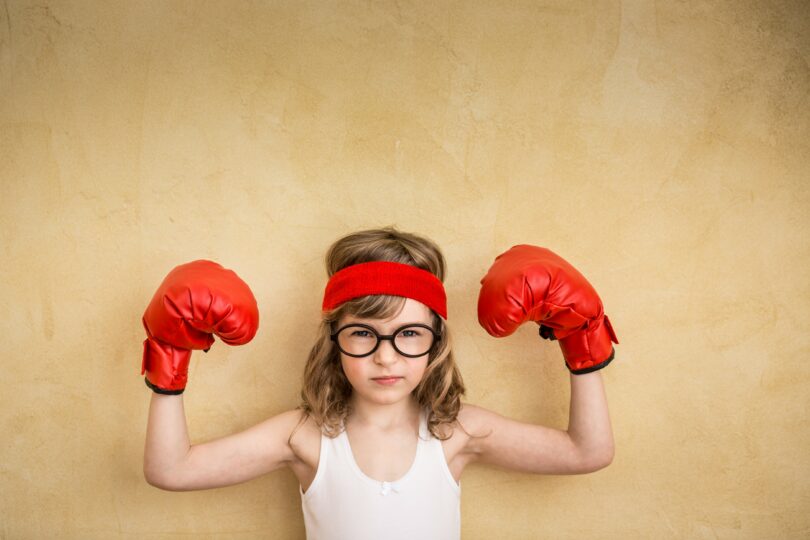 Menina com luvas de boxe e as mãos levantadas em sinal de força.