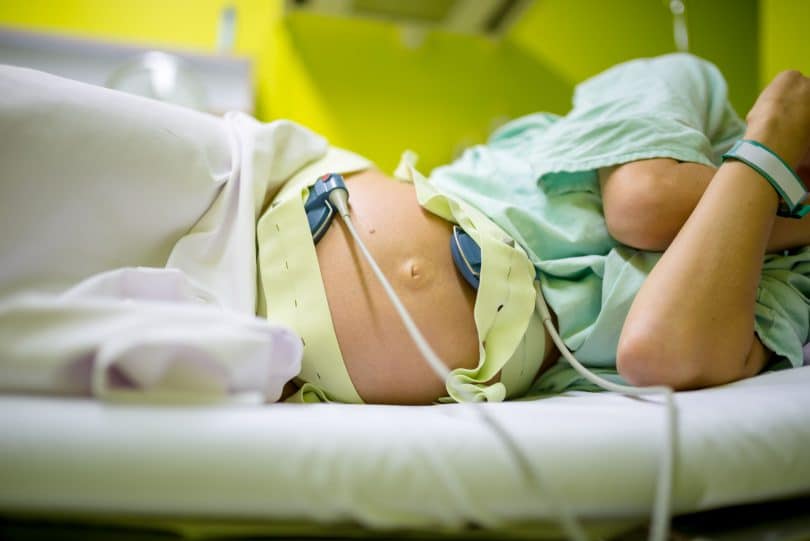 Mulher grávida deitada virada para o lado em uma cama de hospital.