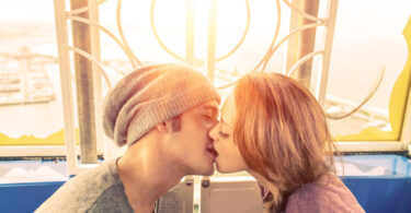 Casal de jovens se beijando em frente a uma janela.