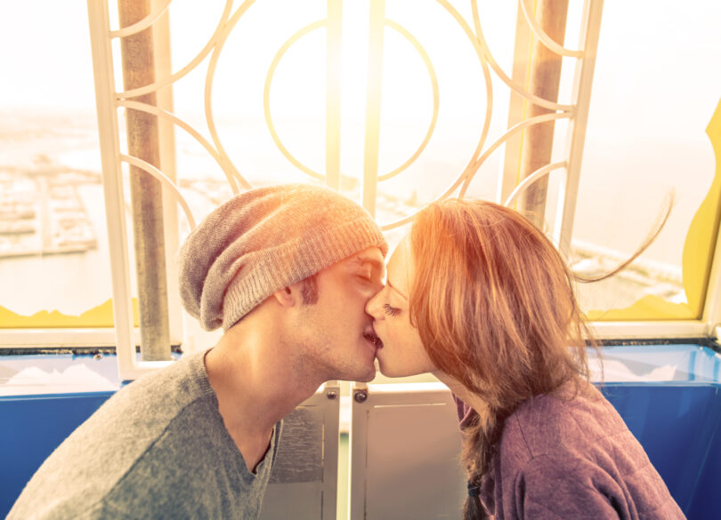 Casal de jovens se beijando em frente a uma janela.