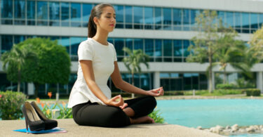 Mulher de negócios praticando yoga perto de prédio comercial.