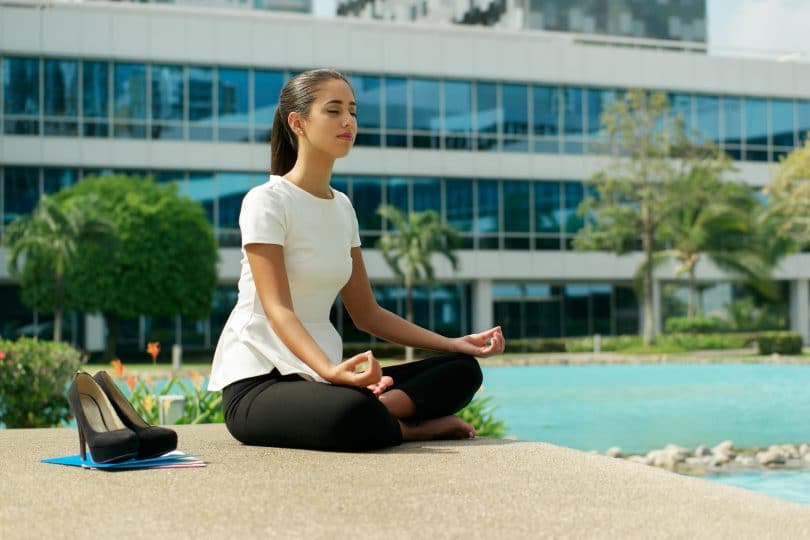 Mulher de negócios praticando yoga perto de prédio comercial.