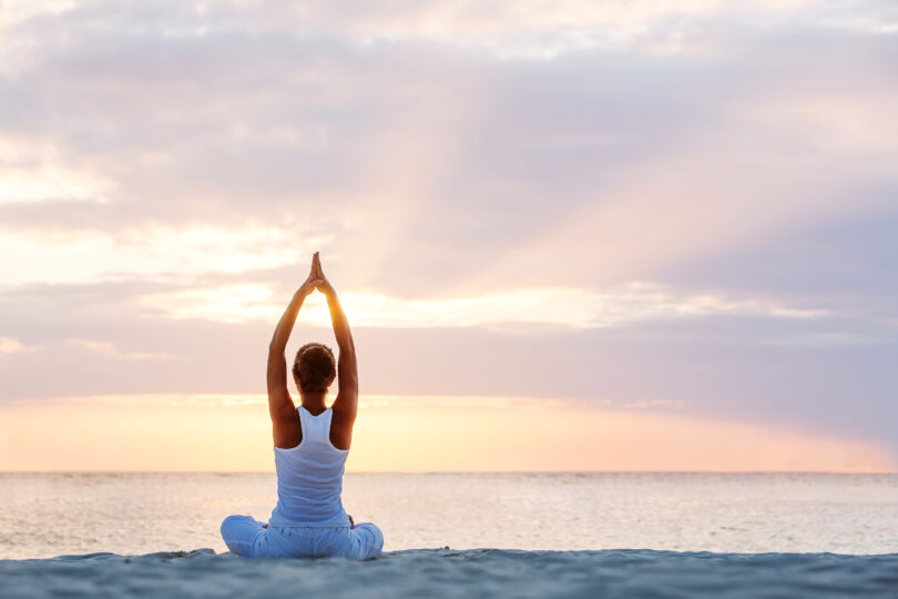 Mulher praticando yoga na beira da praia.