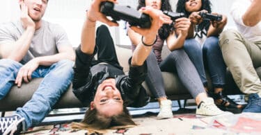 Quatro amigos jovens sentados em um sofá, três deles estão segurando um controle de videogame.