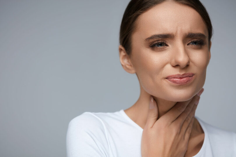 Mulher com mão no pescoço com cara de dor