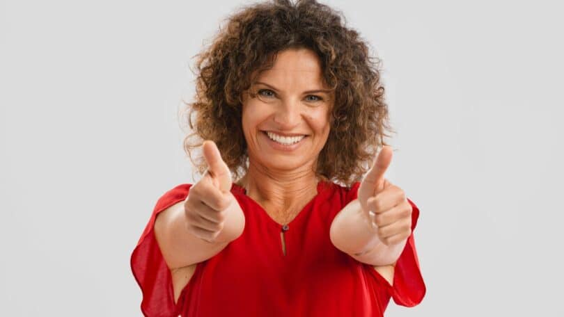 Imagem de uma mulher sorrindo e com as duas mãos fazendo sinal de positivo