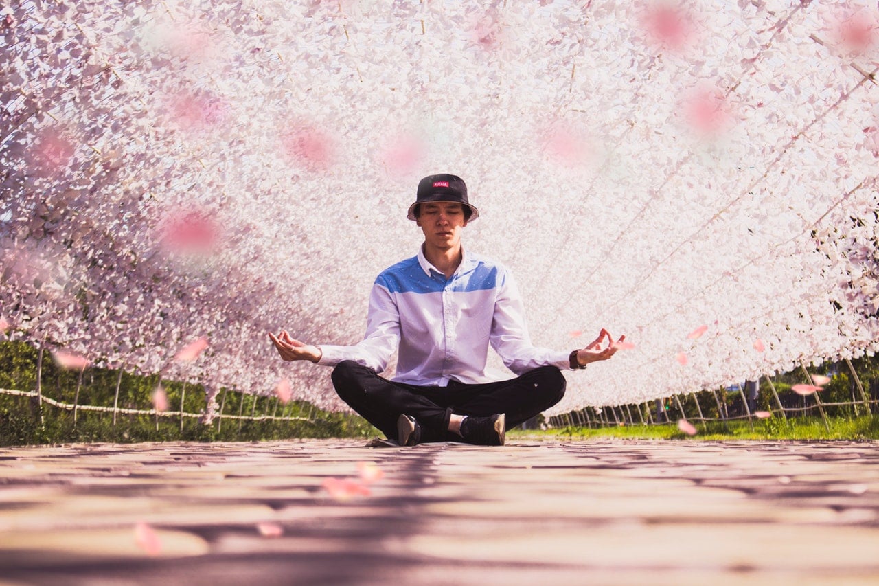 Homem sentado de pernas cruzadas meditando com arcos de flores atrás