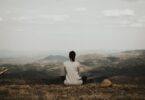 Mulher de costas meditando em uma montanha.