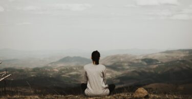 Mulher de costas meditando em uma montanha.