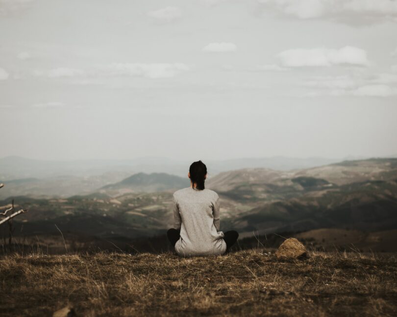 Mulher de costas meditando em uma montanha.