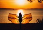 Mulher com "asas" de borboleta em frente ao mar no pôr-do-sol.