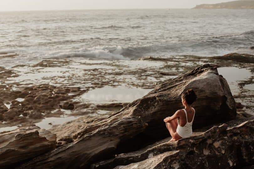 Mulher sentada em uma rocha olhando o mar