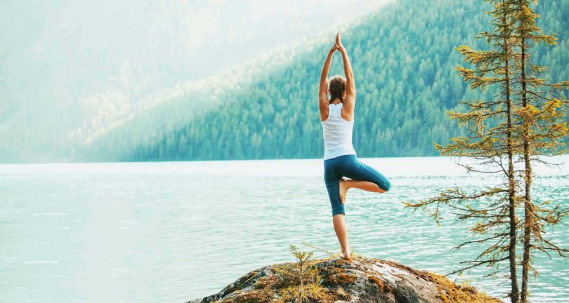 Mulher praticando yoga em frente a um ambiente marcado pela natureza.