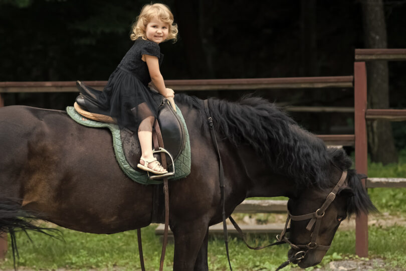 Menina sorrindo em sessão de equoterapia sobre cavalo,