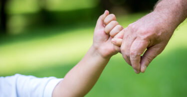 Criança de mãos dadas com adulto em parque.