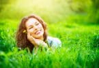 Mulher na grama com mãos o rosto sorrindo e sol refletindo