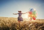 Menina correndo no campo com balões ao pôr do sol.