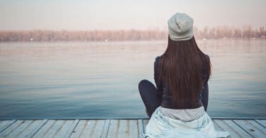 Menina jovem, sentada em um deck de madeira observando o mar.