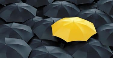 Guarda-chuva amarelo ao lado de guardas-chuvas pretos.