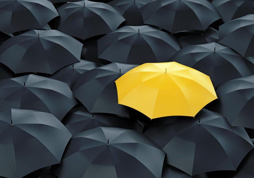 Guarda-chuva amarelo ao lado de guardas-chuvas pretos.