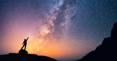 Pessoa com as mãos para o alto em noite estrelada.