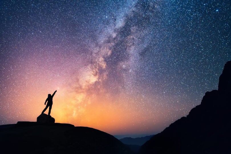 Pessoa com as mãos para o alto em noite estrelada.