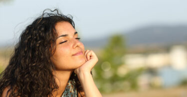 Mulher de olhos fechados iluminada pelo sol