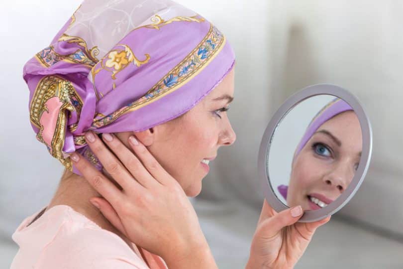 Mulher com bandana na cabeça se olhando no espelho de mão