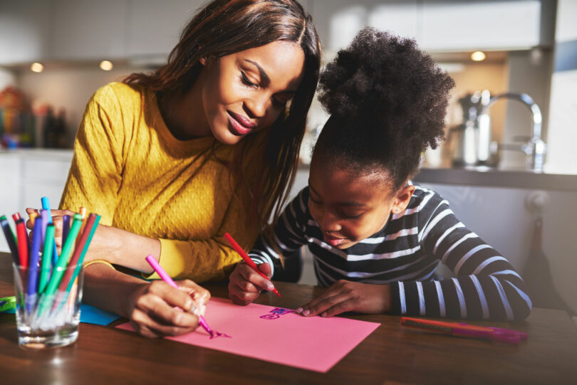 Mãe e filha desenhando em uma folha rosa.