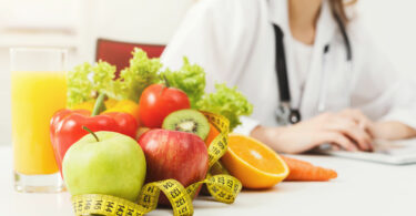 Nutricionista, trabalhando no plano de dieta com frutas e fita métrica na mesa