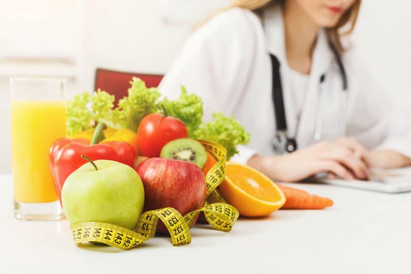 Nutricionista, trabalhando no plano de dieta com frutas e fita métrica na mesa