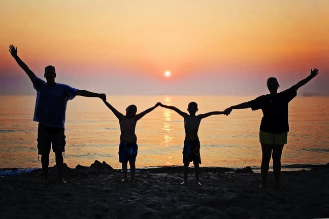 Família de mãos dadas na praia.