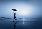 Mulher andando de guarda-chuva na praia à noite.